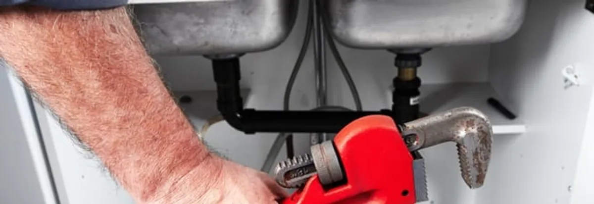 Garbage disposal repair technician tightening drain connections under a kitchen sink in Seattle, WA