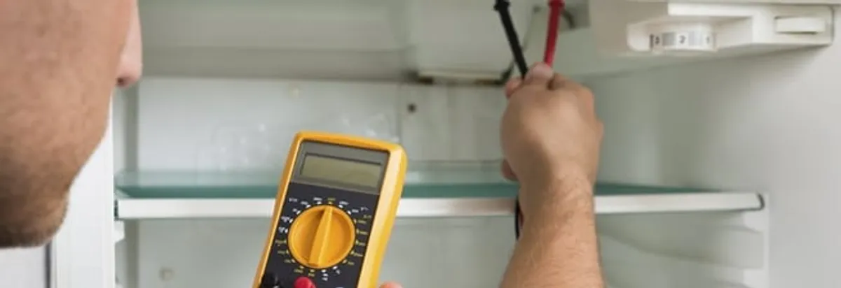 Refrigerator repair technician testing electrical components with a multimeter in Seattle, WA